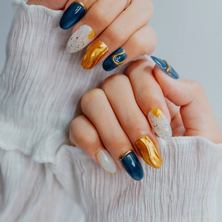 Manucure mêlant bleu marine, feuille d’or et blanc