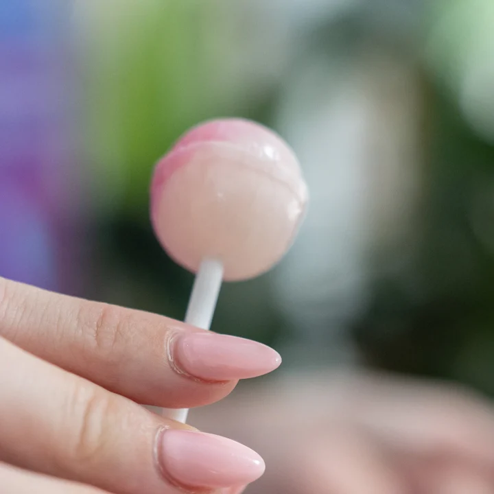Ongles rose pastel tenant une sucette