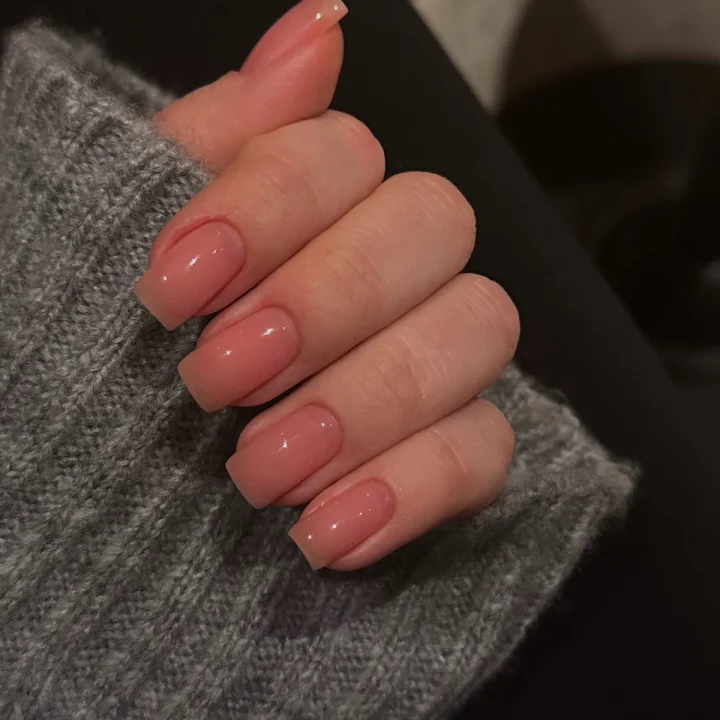Ongles courts rose poudré sur un pull gris